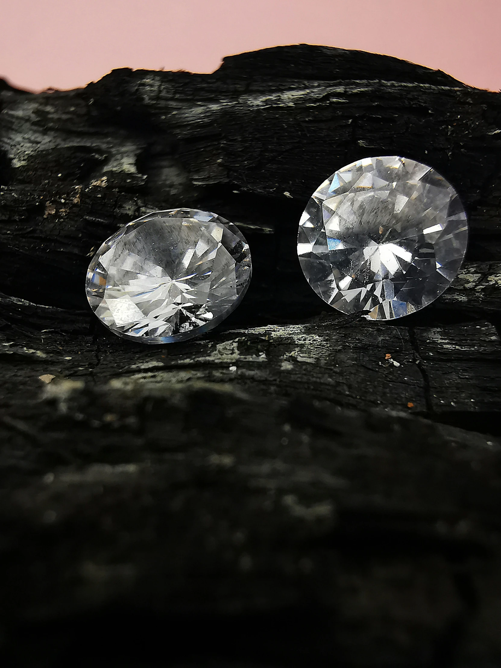 two diamonds sitting on top of a piece of wood, on a dark rock background, photo taken with an iphone, ((rocks)), platinum jewellery