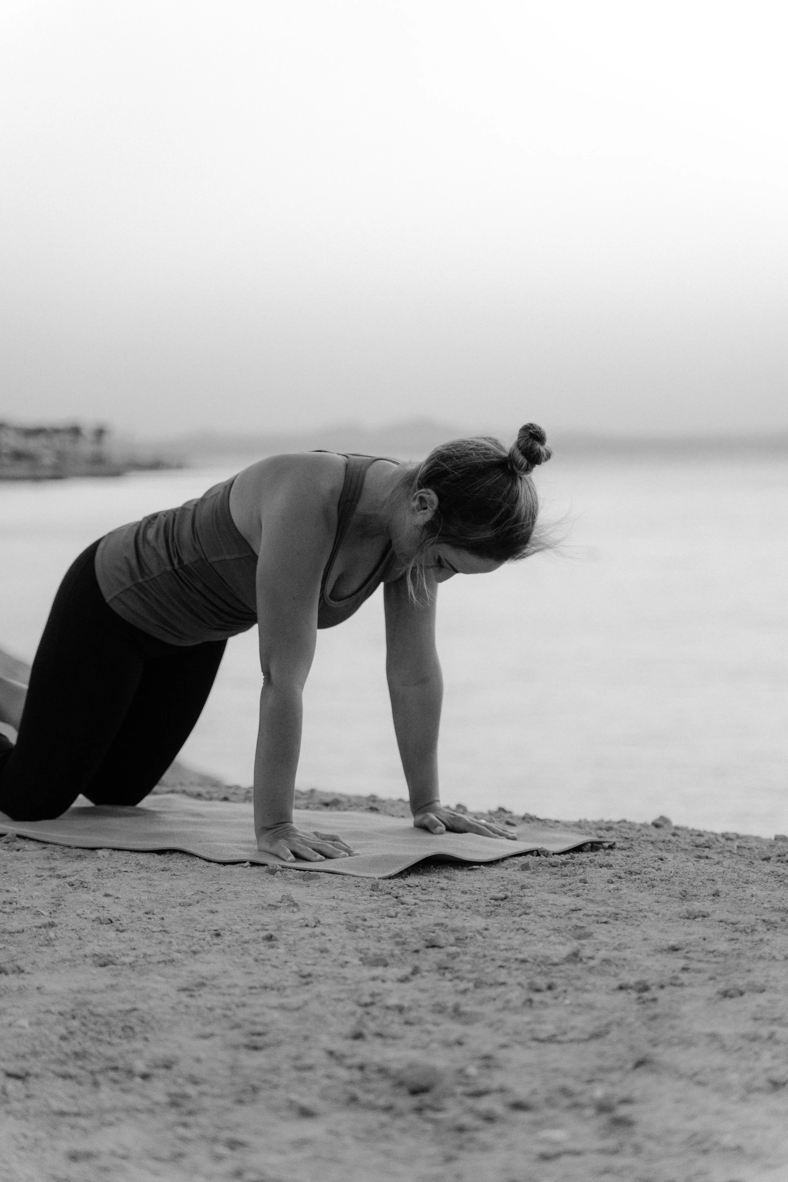 a woman doing a yoga pose on the beach, a black and white photo, crawling on the ground, in egypt, working out, profile image