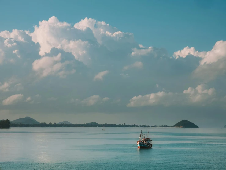 a boat floating on top of a large body of water, a picture, unsplash contest winner, dramatic clouds cyan atmosphere, fishing boat, hd footage, tropical climate