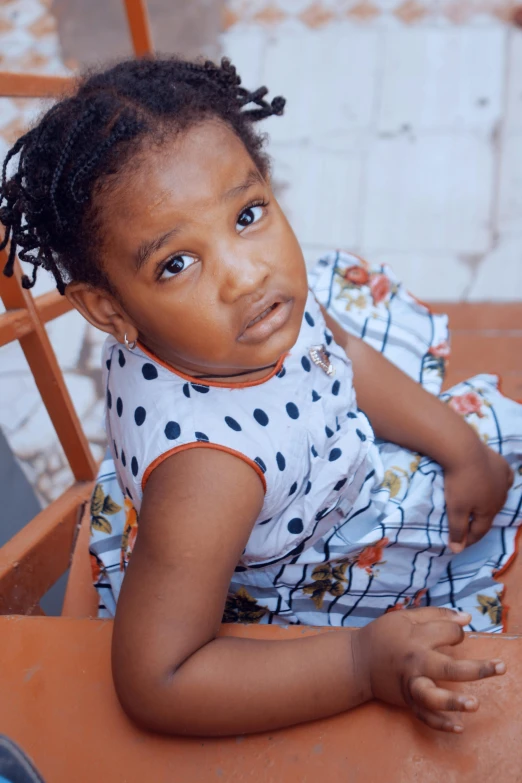 a little girl sitting on top of a wooden chair, by Chinwe Chukwuogo-Roy, pexels contest winner, looking down on the camera, gif, wearing a dress, toddler