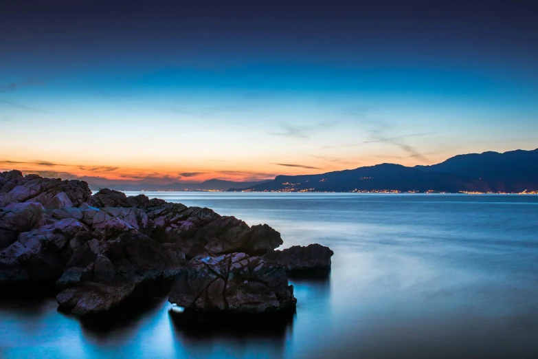 a group of rocks sitting on top of a body of water, by Alexis Grimou, sunset panorama, blue sea, split near the left, night-time