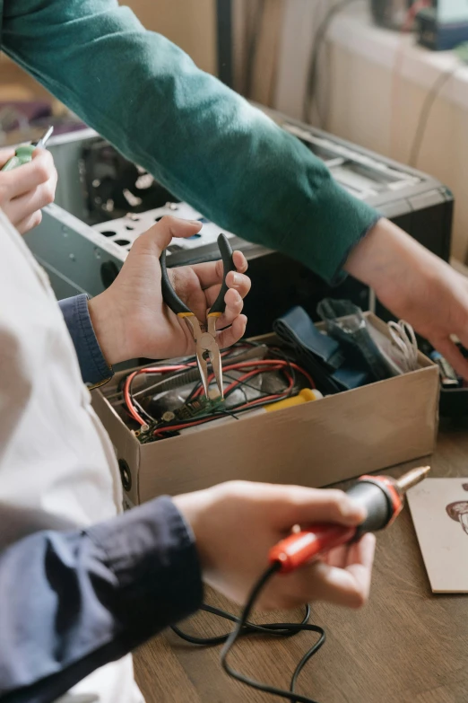 a couple of people that are working on something, by Niko Henrichon, trending on pexels, electrical case display, batteries not included, tools for science research, brown