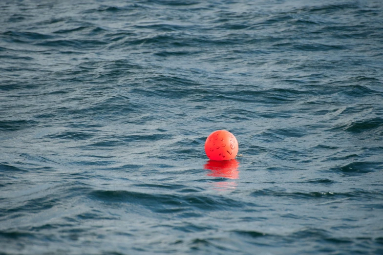 a red buoy floating on top of a body of water, in the ocean, playing