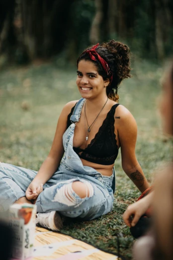 a group of people sitting on top of a grass covered field, justina blakeney, wearing a bandana and chain, she is wearing a black tank top, torn overalls