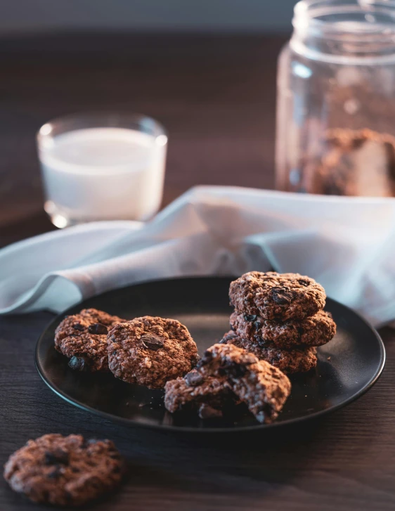 a black plate topped with cookies next to a glass of milk, by Julia Pishtar, unsplash, dau-al-set, chocolate, big oatmeal, gif, buds