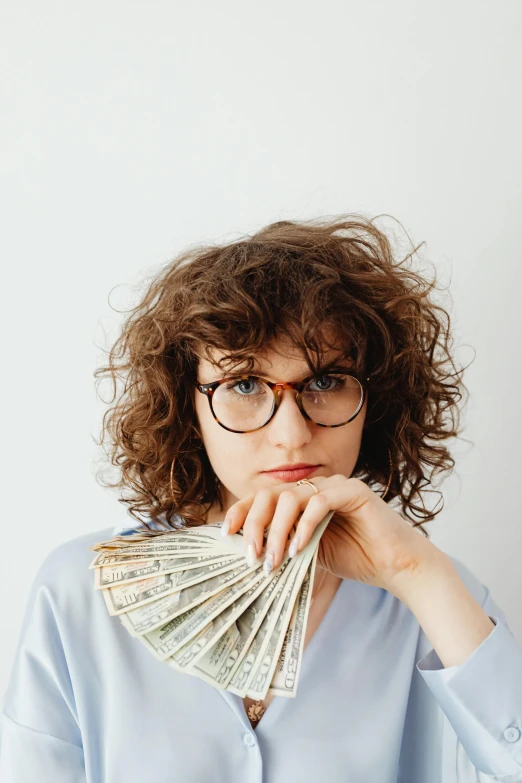 a woman holding a fan of money in front of her face, pexels contest winner, square rimmed glasses, curly bangs, proportional image, half image