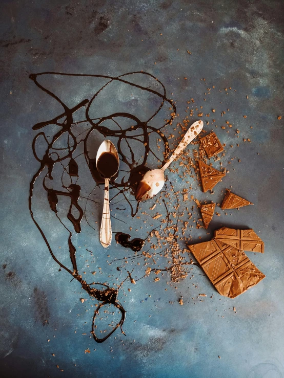 a piece of chocolate sitting on top of a table, a still life, inspired by William Michael Harnett, pexels contest winner, surrealism, splattered tar, spatula, a portrait of @hypnos_onc, blue