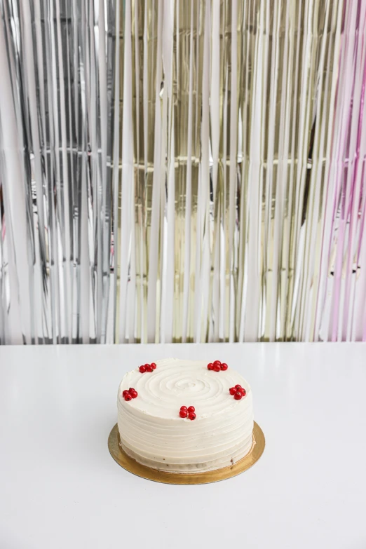 a white cake sitting on top of a table, a picture, in front of white back drop, red wires wrap around, tin foiling, background bar