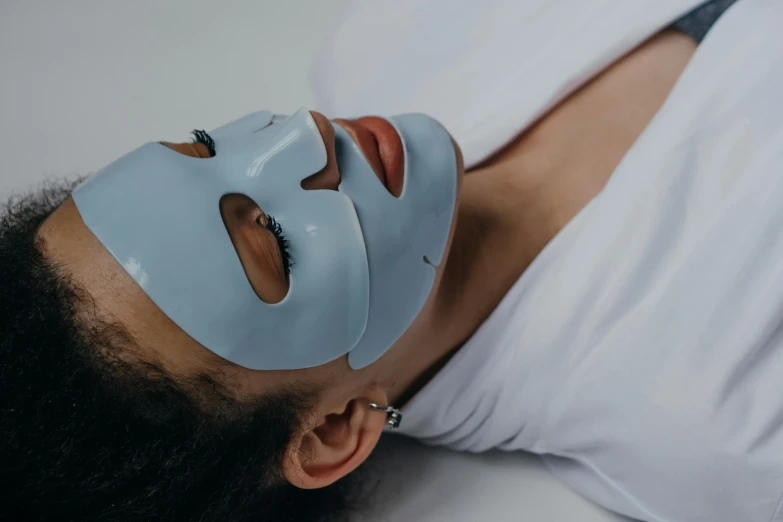 a woman laying down with a mask on her face, profile image, grey, sapphire, manuka