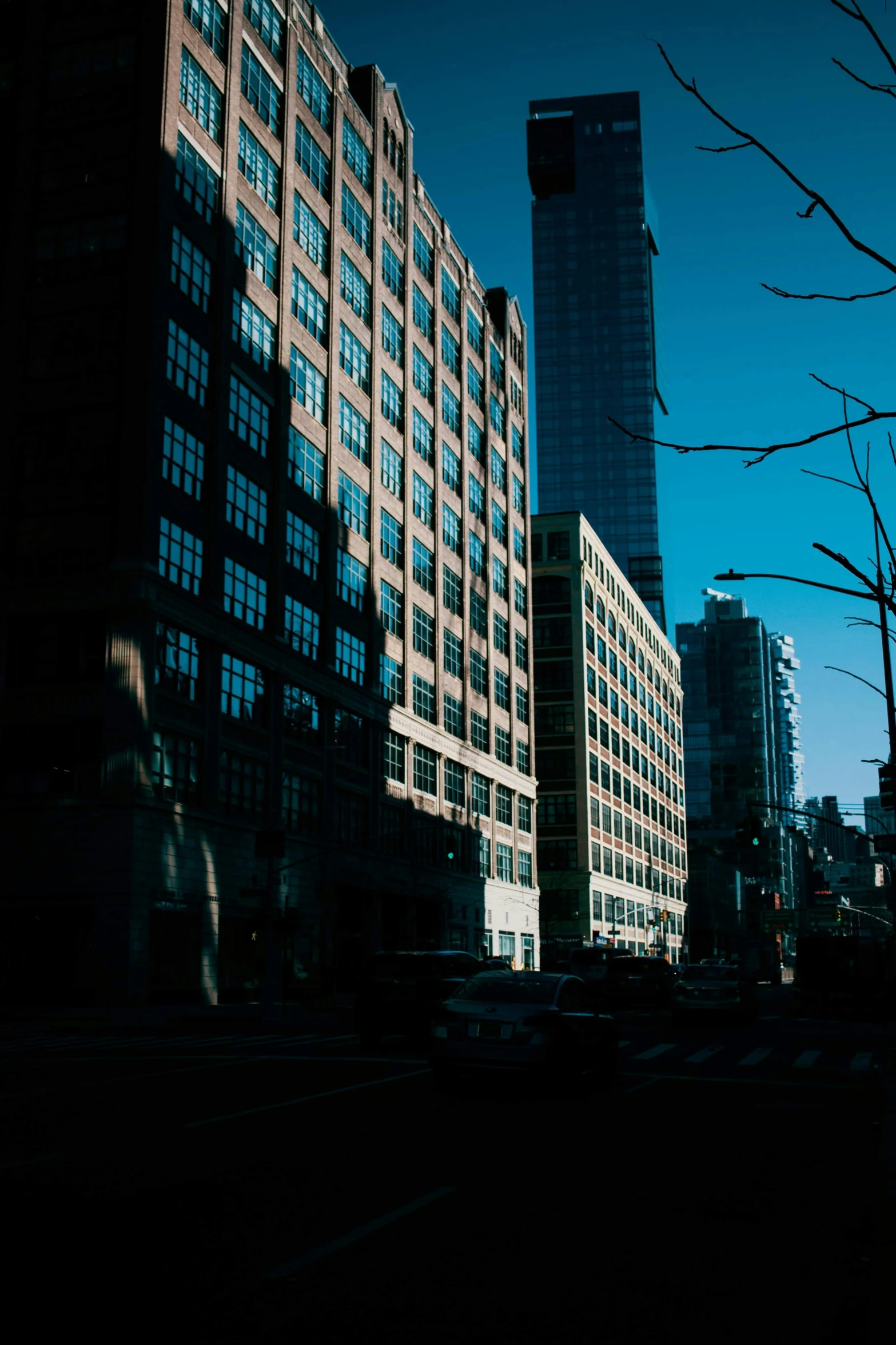 a man riding a skateboard down a street next to tall buildings, a picture, inspired by Elsa Bleda, unsplash, big shadows, new - york skyline in winter, low quality photo, cinematic shot ar 9:16 -n 6 -g