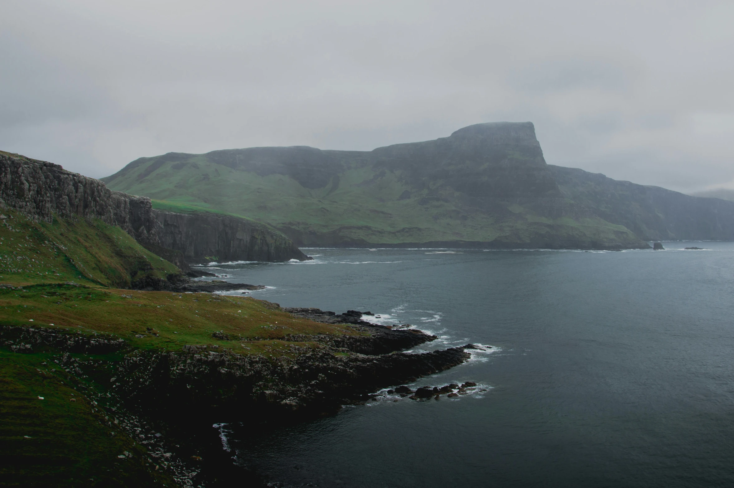 a body of water with a mountain in the background, a picture, pexels contest winner, hurufiyya, coastal cliffs, rainy and foggy, highlands, panoramic