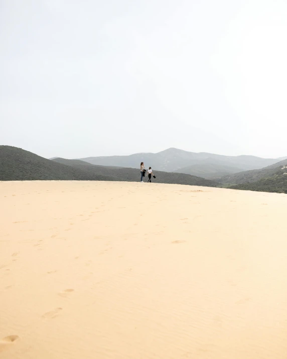 two people standing on top of a sand dune, by Arabella Rankin, unsplash contest winner, over the hills, very buff, sandy beige, white beaches