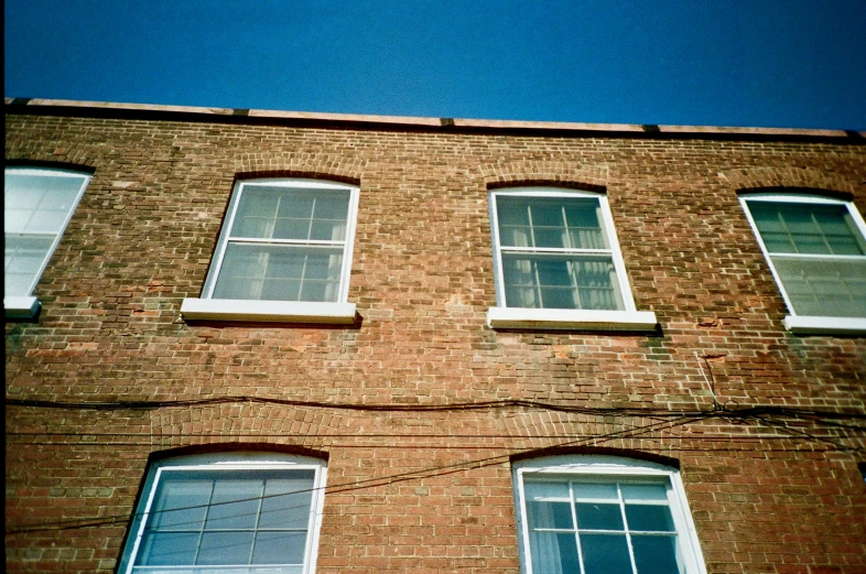 a tall brick building with lots of windows, an album cover, inspired by Thomas Struth, unsplash, postminimalism, fuji superia, blue sky, cracked windows, taken from the high street