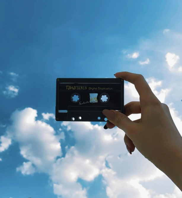 a person holding up a cassette in front of a blue sky, pexels contest winner, aestheticism, the sky is black, palace floating in the sky, synth, cotton clouds