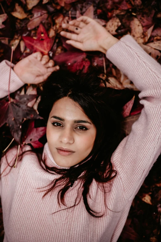 a woman laying on top of a pile of leaves, a picture, by irakli nadar, trending on pexels, young himalayan woman, wearing a sweater, headshot, pink