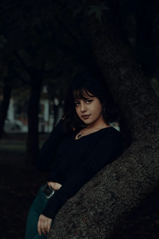 a woman leaning against a tree in a park, inspired by Elsa Bleda, pexels contest winner, realism, dark hair, 🤤 girl portrait, wearing a dark sweater, low - lighting
