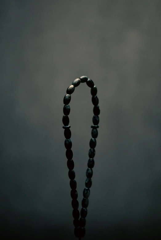 a close up of a rosary on a table, an album cover, unsplash, nadav kander, dark. no text, standing straight, panel of black