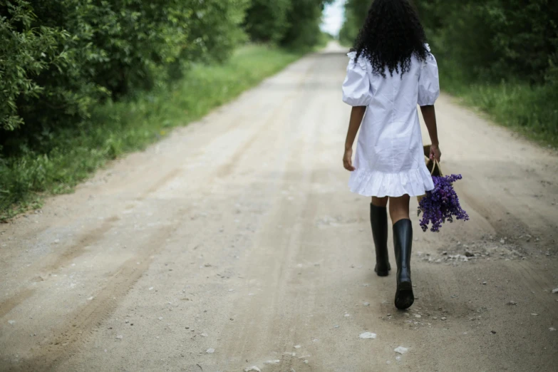 a woman walking down a dirt road holding a bunch of flowers, inspired by Andrew Wyeth, pexels contest winner, magic realism, black girl, white blouse and gothic boots, purple eyes and white dress, wearing maid uniform