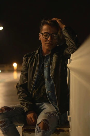 a man sitting on a ledge at night, by Robbie Trevino, she wears leather jacket, with glasses, grainy footage, ariel perez