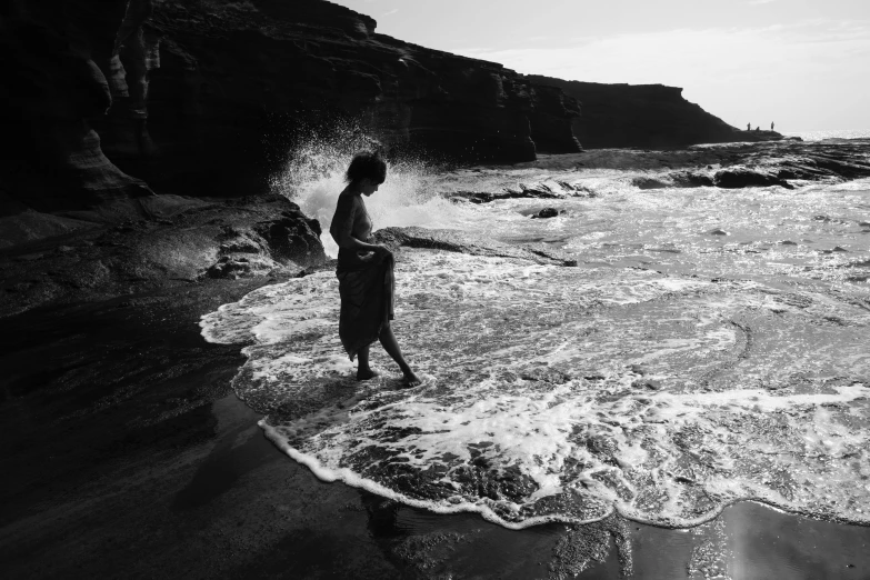 a man standing on top of a beach next to the ocean, a black and white photo, unsplash, conceptual art, playing in waterfalls, kara walker, children playing at the beach, erosion