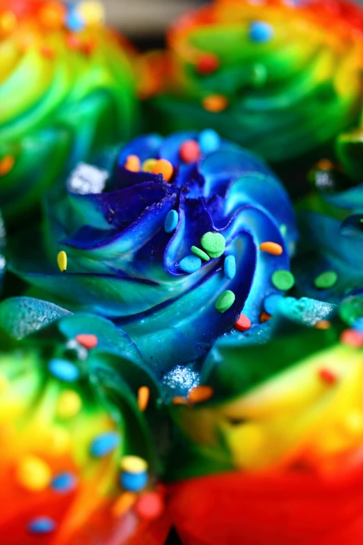 a close up of a rainbow cupcake with sprinkles, inspired by Daniel Schultz, deep blue sea color, swirly curls, greens and blues, made of wax and water