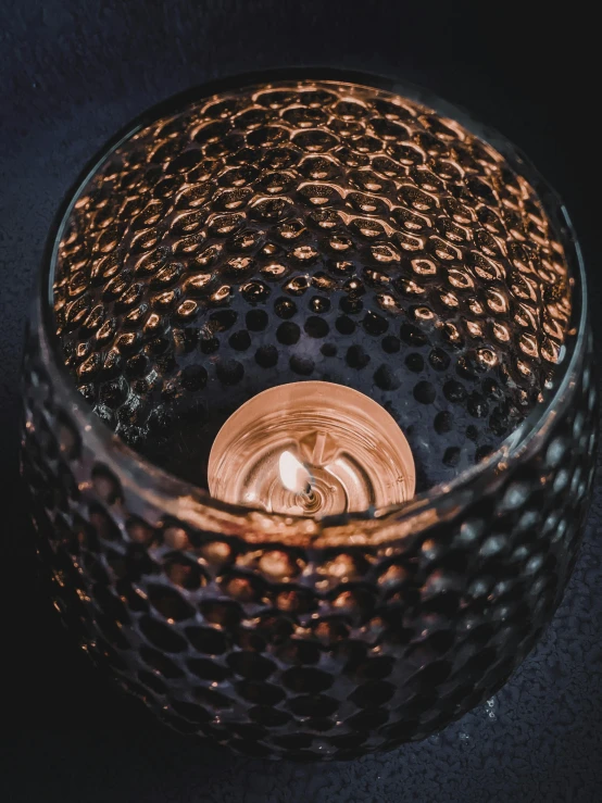 a lit candle sitting on top of a table, inspired by Yayou Kusama, renaissance, black textured, reflections in copper, macro lens product photo, made of glazed