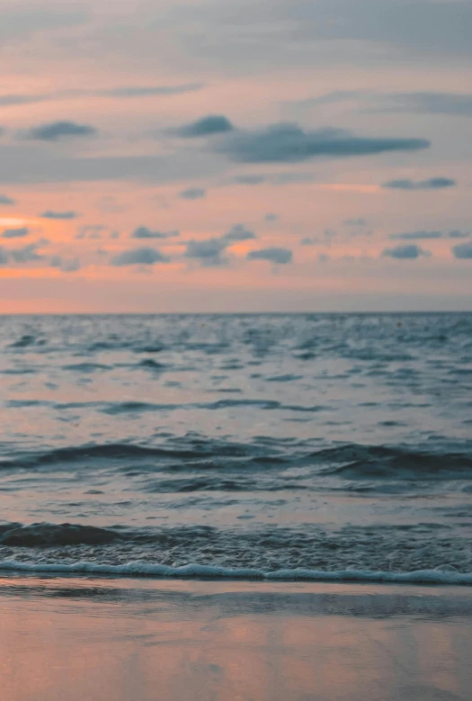 a man riding a surfboard on top of a sandy beach, during a sunset, body of water, in the ocean