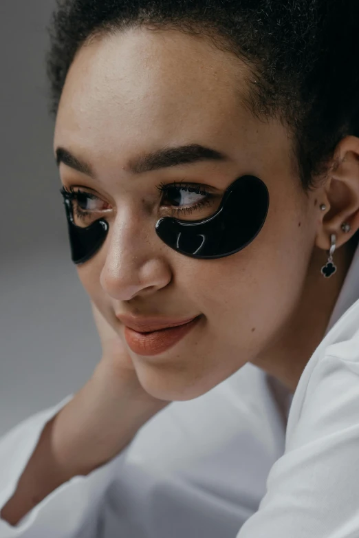 a woman with black eye patches on her face, by Julia Pishtar, trending on pexels, hurufiyya, photoshoot for skincare brand, wavy, wearing shiny black goggles, her face in discs