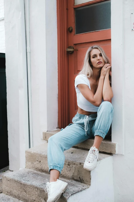 a woman sitting on the steps of a building, by Robbie Trevino, trending on pexels, baggy jeans, white blonde hair, standing in corner of room, wearing crop top