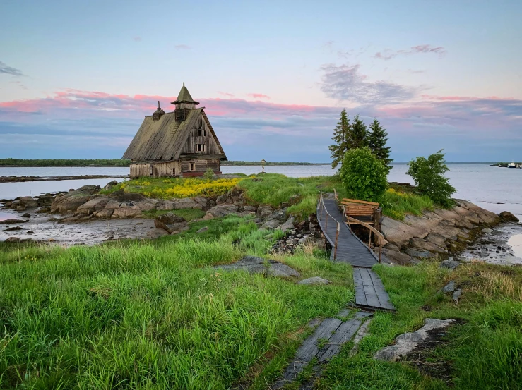 a small wooden building sitting on top of a lush green field, inspired by Einar Hakonarson, romanticism, near a jetty, pink golden hour, churches, stone pathways