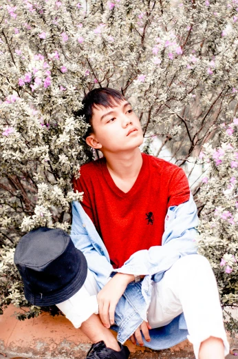 a young man sitting in front of a bush of flowers, an album cover, inspired by Chen Chi, unsplash, portrait androgynous girl, red colored, avatar image, casually dressed