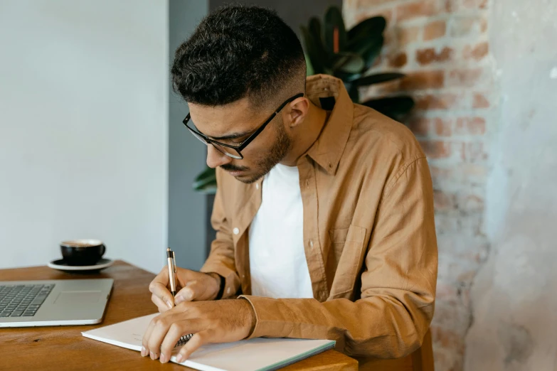 a man sitting at a table writing in a notebook, pexels contest winner, brown shirt, ashteroth, thumbnail, aboriginal australian hipster