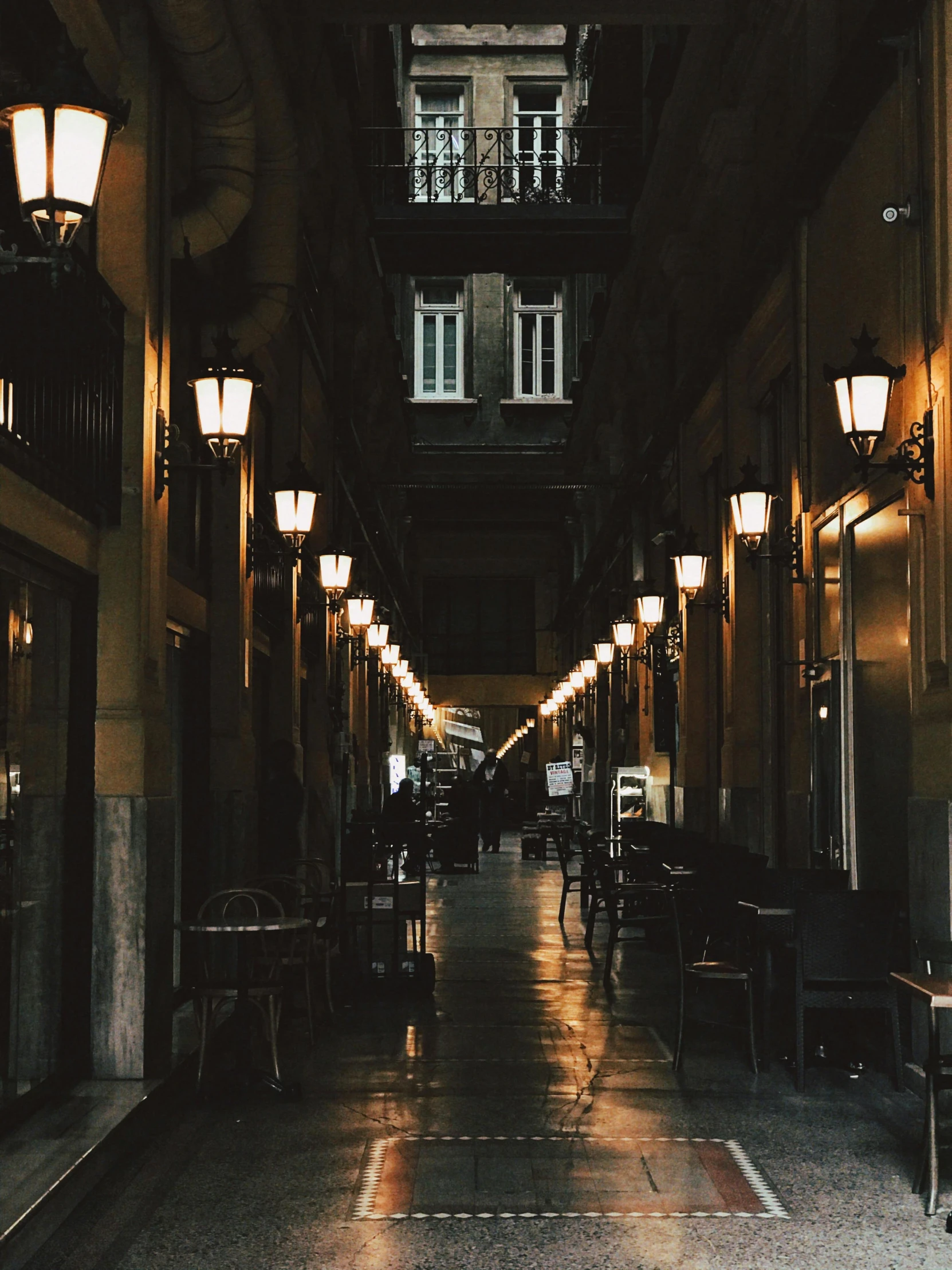 a narrow street lined with tables and chairs, an album cover, by Alejandro Obregón, unsplash contest winner, neoclassicism, it's getting dark, profile image, dark university aesthetic, street lanterns glow