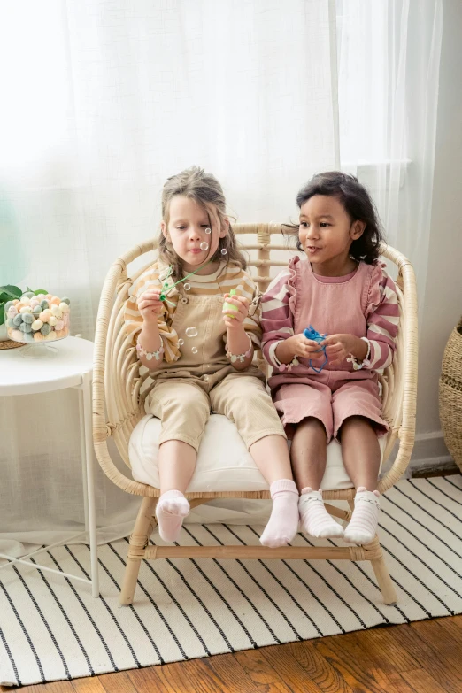 two little girls sitting on a wicker chair, trending on instagram, having a snack, diverse outfits, designed for cozy aesthetics!, promotional photo
