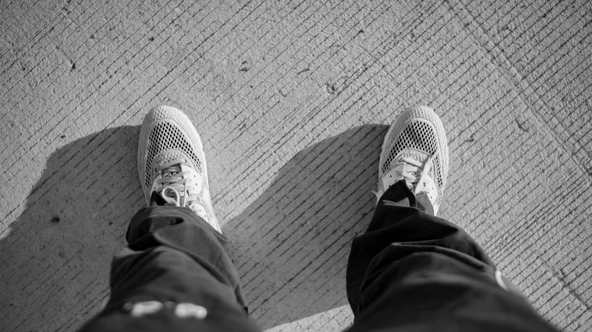 a black and white photo of a person's feet, by Niko Henrichon, unsplash, wearing white sneakers, looking straight to camera, paved, crosshatch