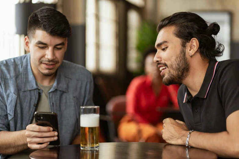 two men sitting at a table looking at a cell phone, trending on pexels, happening, a pint of beer sitting on a bar, aussie baristas, young spanish man, avatar image