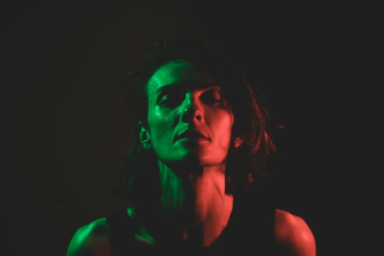 a woman with a green light on her face, an album cover, inspired by Anna Füssli, pexels contest winner, bauhaus, dramatic lighting and colors, sigourney weaver, dark. studio lighting, portrait of head and body