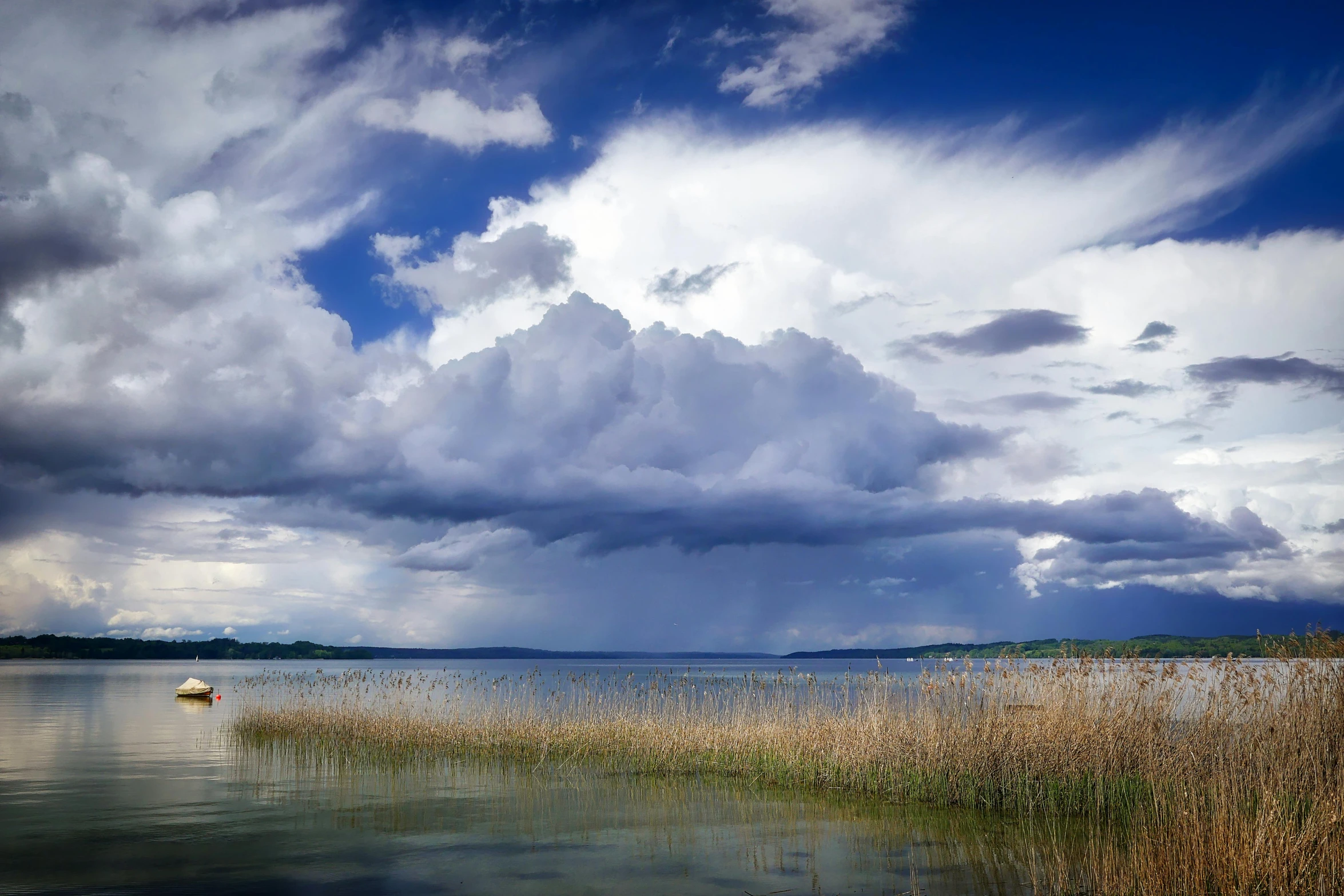 a boat floating on top of a lake under a cloudy sky, by Jan Rustem, towering cumulonimbus clouds, reeds, nature photograph, lake blue
