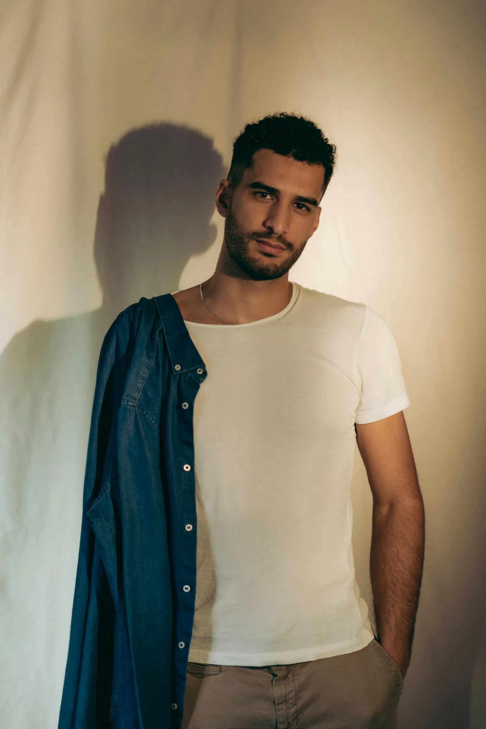 a man standing in front of a white wall, an album cover, borja, dressed in a white t-shirt, photo of a model, elias chatzoudis