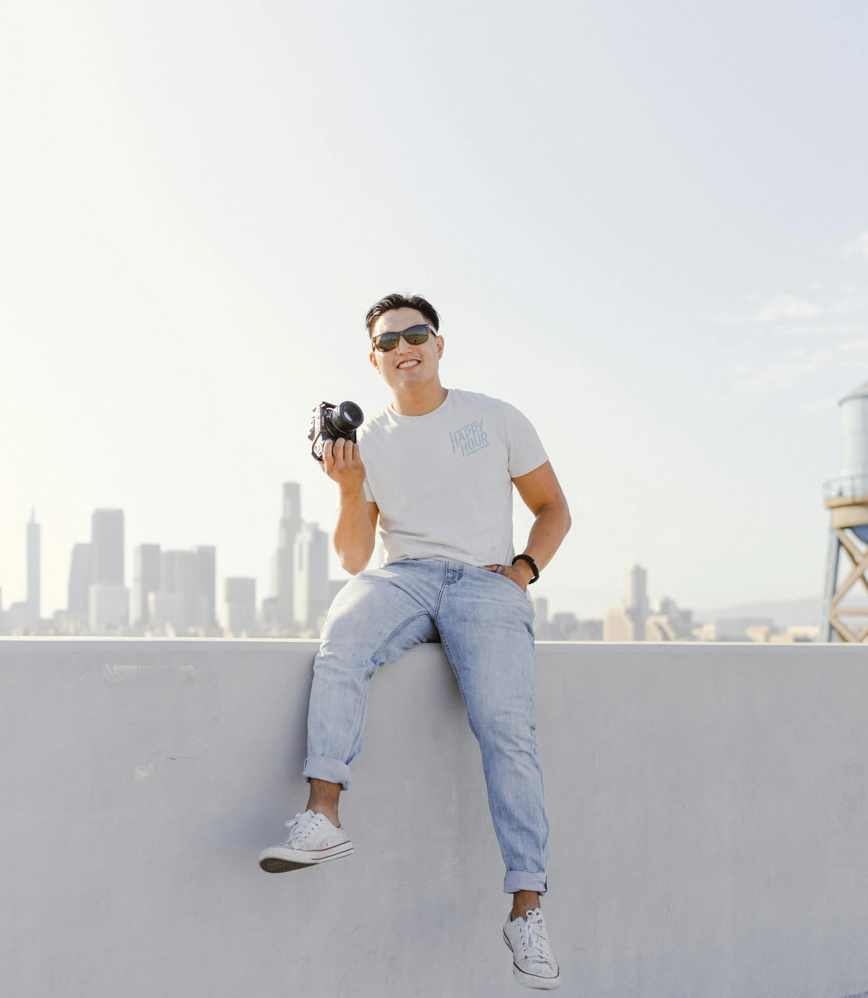 a man sitting on a wall holding a camera, by Robbie Trevino, avatar image, low quality photo, city backdrop, stanley lau