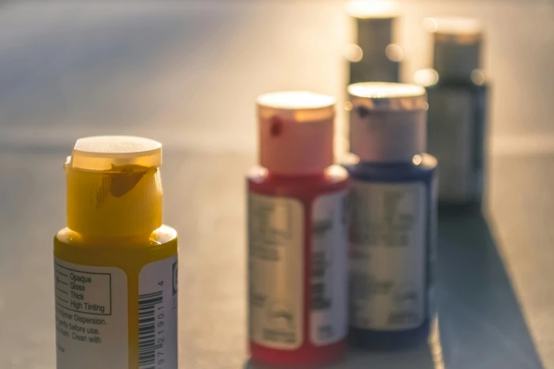 a close up of a bottle of paint on a table, pexels contest winner, medical labels, sunrise colors, bottles, different sizes