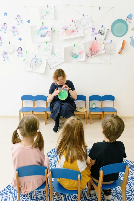 a woman sitting in front of a group of children, a picture, inspired by Elsa Beskow, pexels contest winner, danube school, indoor picture, 15081959 21121991 01012000 4k, facing away, crafts