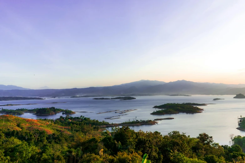 a large body of water surrounded by trees, sumatraism, mountains and lakes, islands on horizon, sun down, expansive view