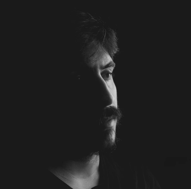 a black and white photo of a man with a beard, a black and white photo, by Adam Marczyński, pexels contest winner, conceptual art, vantablack chiaroscuro, colin greenwood (bass), discord profile picture, sad lighting