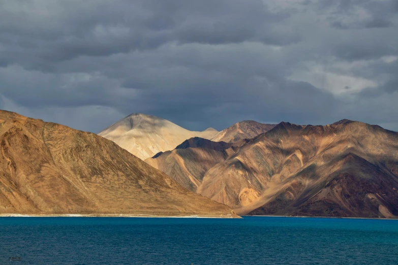 a body of water surrounded by mountains under a cloudy sky, by Peter Churcher, hurufiyya, conde nast traveler photo, multicoloured, fan favorite, india