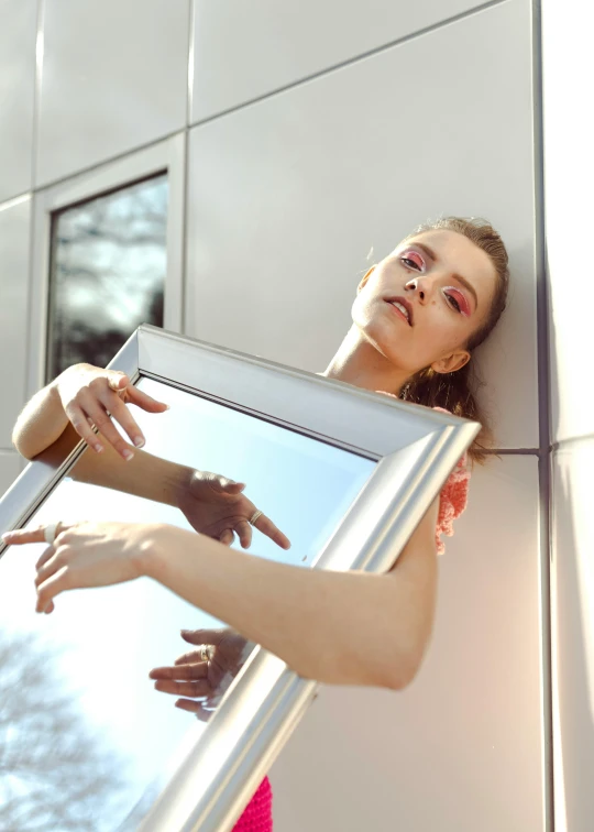 a woman holding a picture in front of a mirror, inspired by Elsa Bleda, pexels contest winner, surrealism, in sunny weather, non binary model, person made out of glass, sassy pose