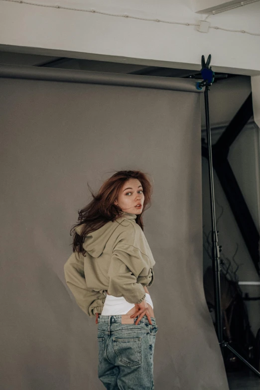 a woman standing in front of a gray backdrop, a picture, by Jason Chan, trending on pexels, bae suzy, in an action pose, looking back at the camera, studio backdrop