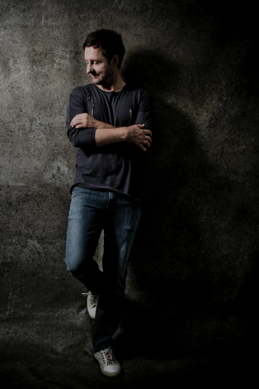 a man leaning against a wall with his arms crossed, a portrait, inspired by Dennis Miller Bunker, pexels contest winner, keanu reeves, dark grey backdrop studio, fullbody of standing tom selleck, a high angle shot