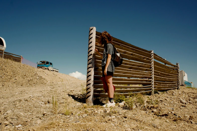 a woman leaning against a fence in the desert, unsplash, land art, vehicle, cut into the side of a mountain, ash thorp, construction