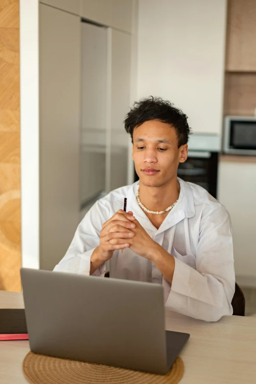 a man sitting at a table in front of a laptop, wearing white pajamas, ashteroth, with accurate features, thumbnail